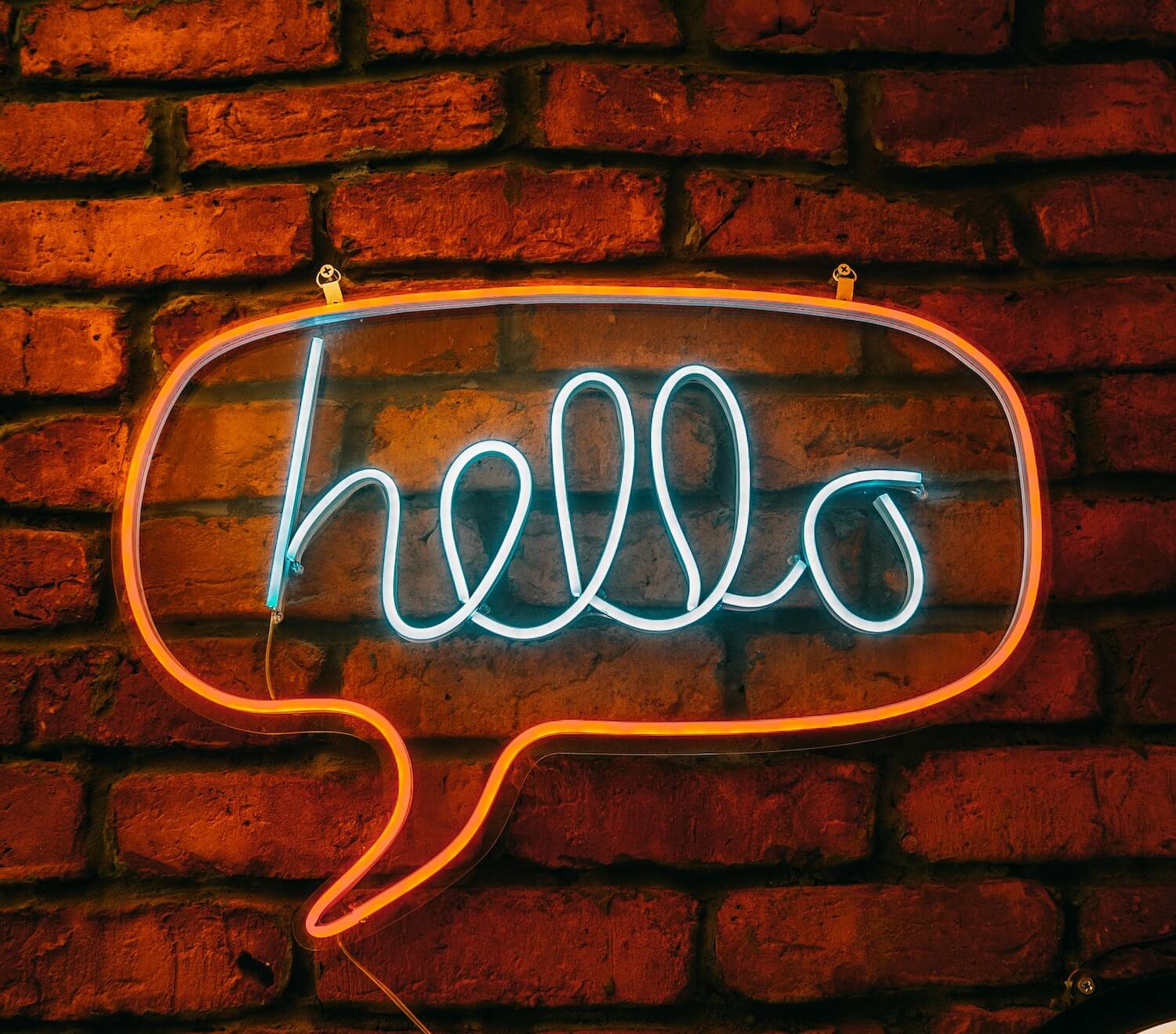A brick wall with a neon sign hung on it that says "hello" in a speech bubble