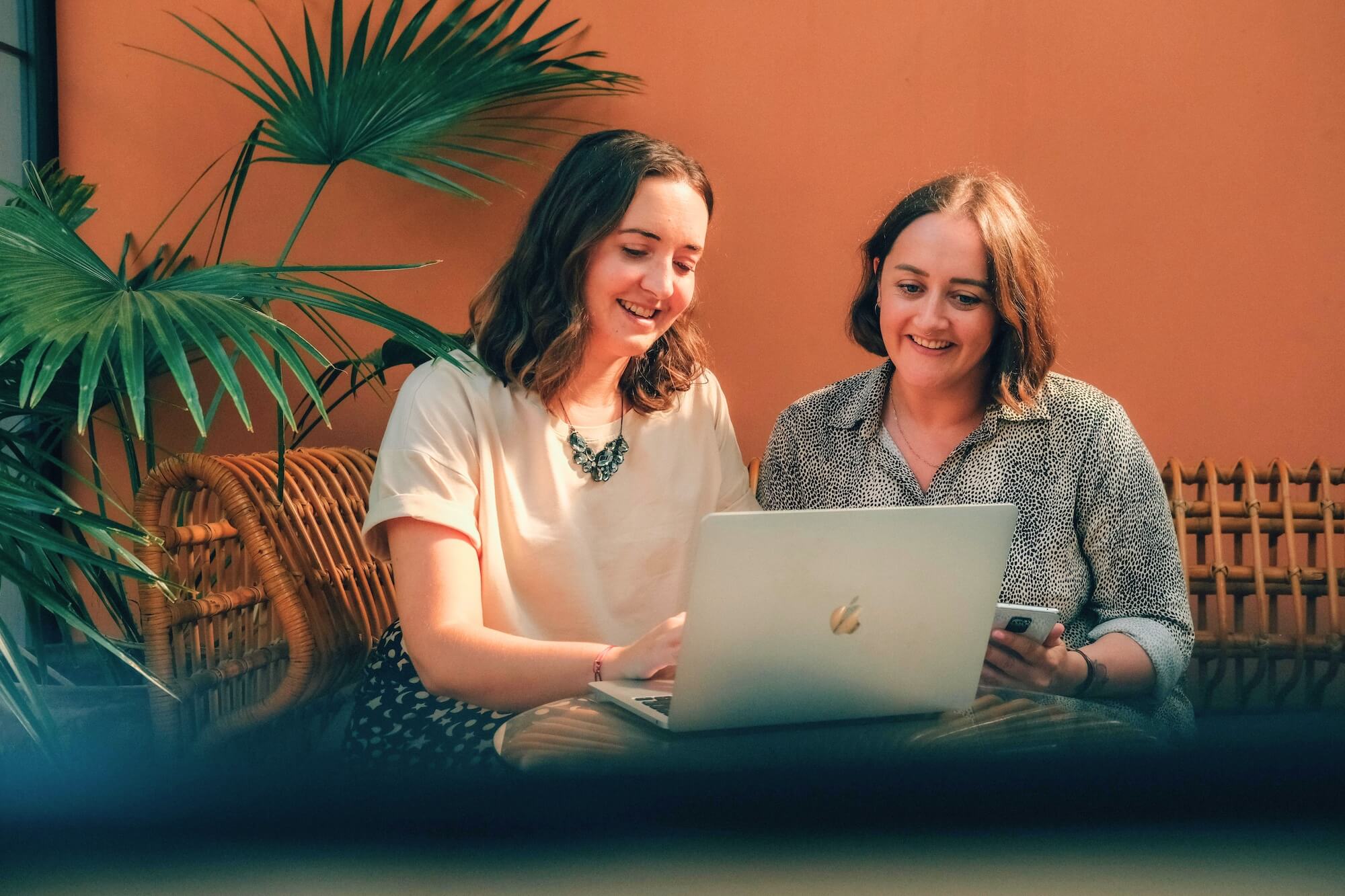 Holly Close & Sophie Bellamy, two women with brown hair look at a MacBook on a coffee table