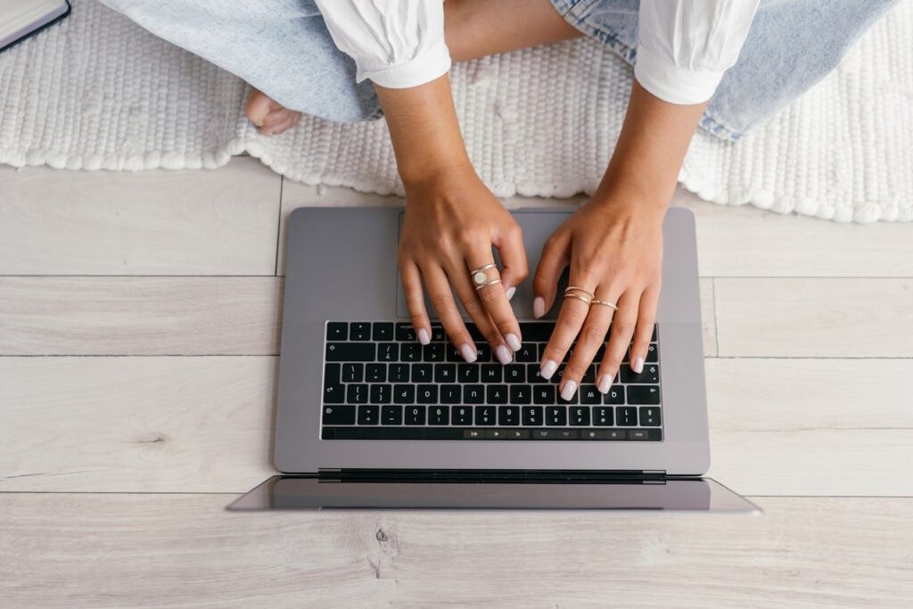 A person sitting cross-legged on a white rug typing on a laptop